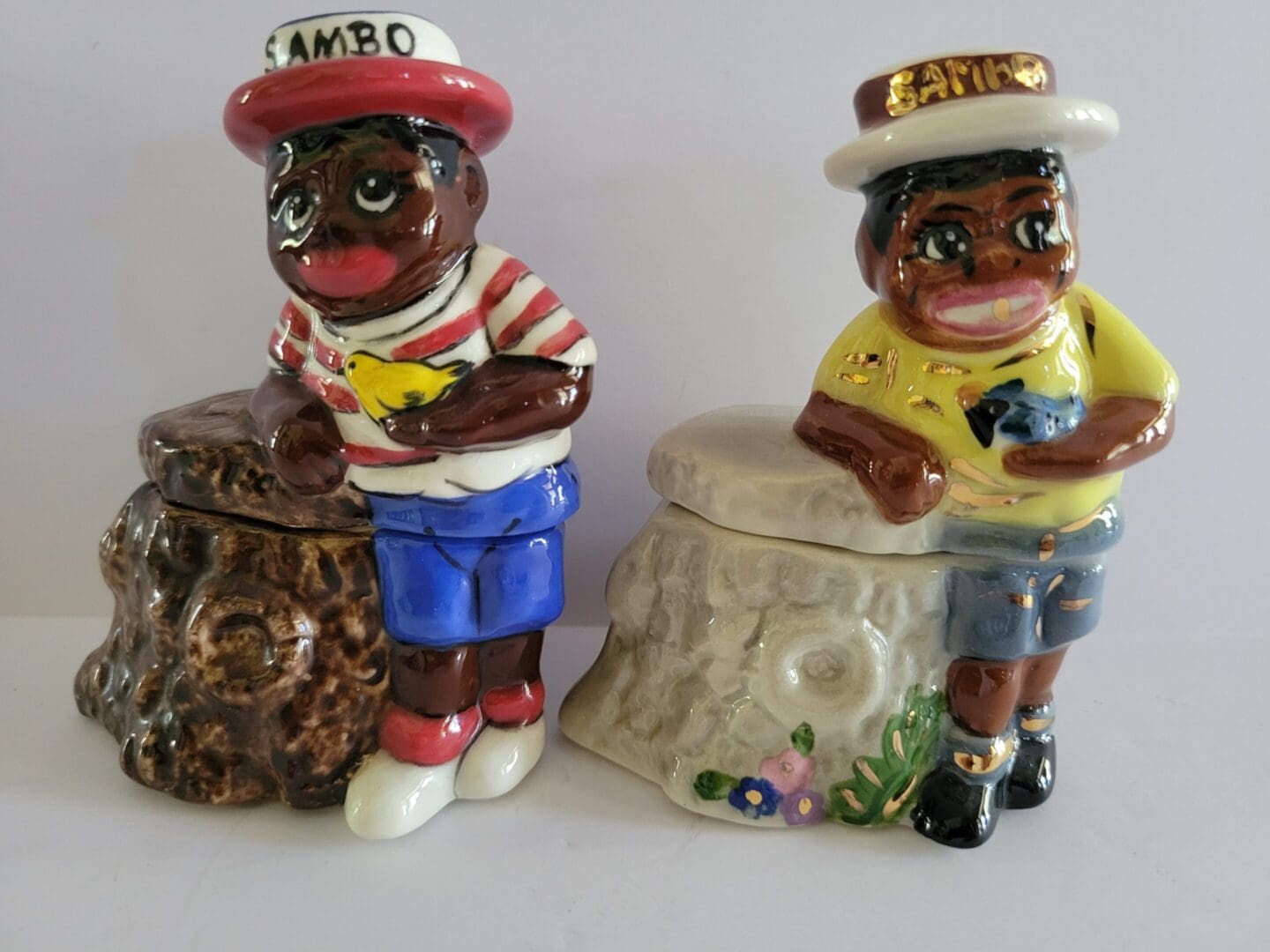 Two ceramic figures with hats on tree stumps.