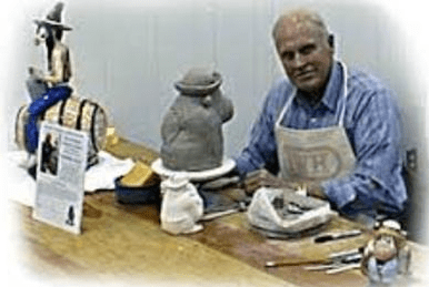 Man sculpting ceramic figure in workshop.