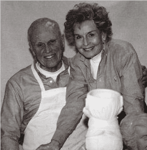 Smiling couple wearing aprons in a black and white photo.