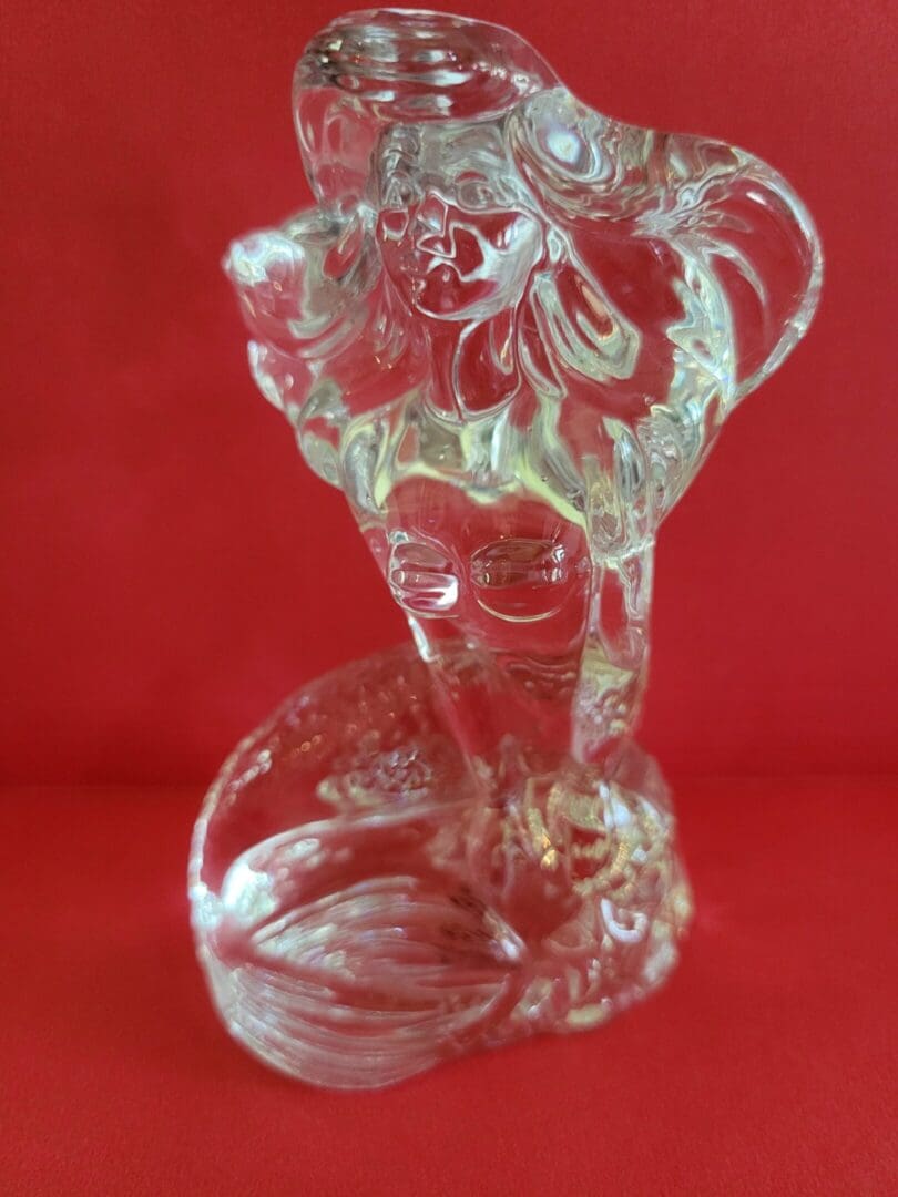 Glass mermaid figurine on red background.