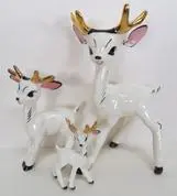 Three white porcelain deer figurines with gold antlers.