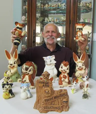 Man holding figurines with "Twin Winston Creations" sign.