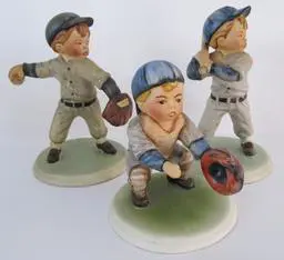 Three ceramic figurines of boys playing baseball.