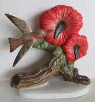 Hummingbird figurine with red flowers on branch.