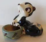 Ceramic figurine of a skunk holding a bowl.