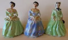 Three porcelain figurines of women in gowns.