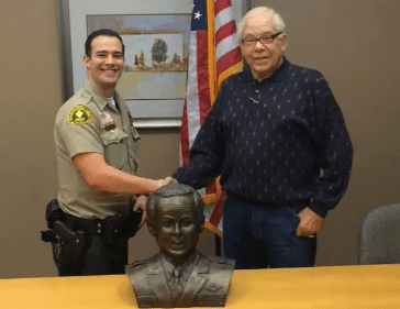 Two men shaking hands in front of a bust.